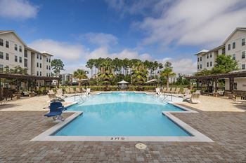 A large swimming pool surrounded by a brick patio and lounge chairs.